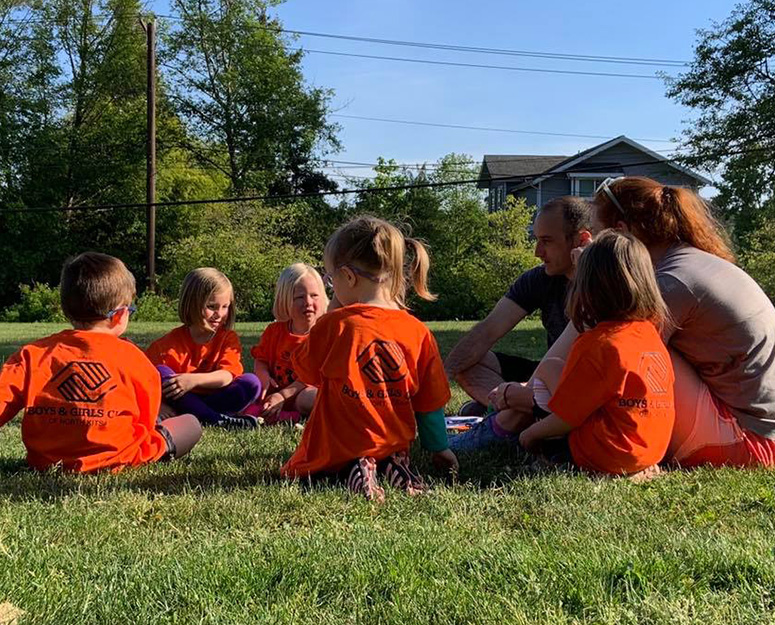 nkitsap_childcare North Kitsap group of young children sitting in circle on grass with 2 adults