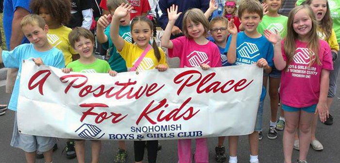 group of kids smiling and waving holding boys & girls club banner