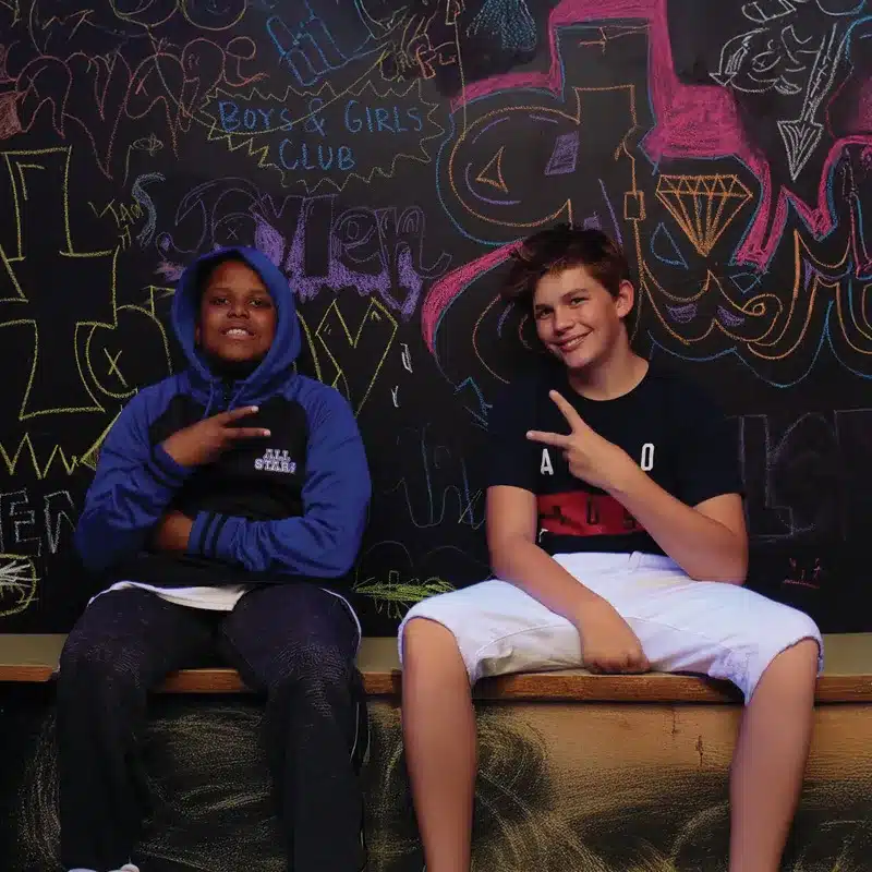 2 teen boys sitting in front of graffiti chalkboard