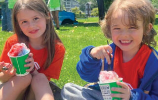 Two girls sitting on grass eating ices
