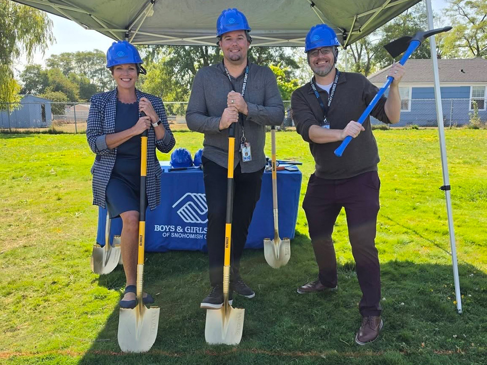 3 men in blue hardhats with shovels on green grass lawn